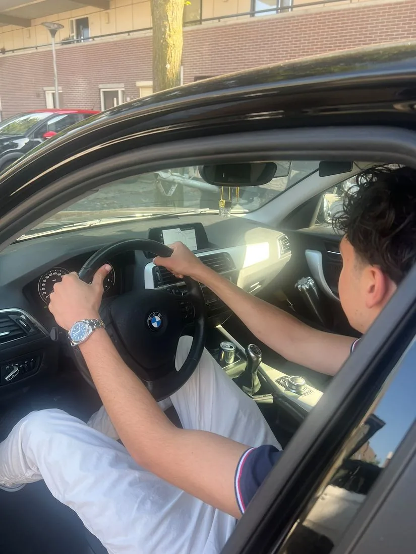 Leerling met beide handen aan het stuur van de lesauto, gezien door het geopende portier