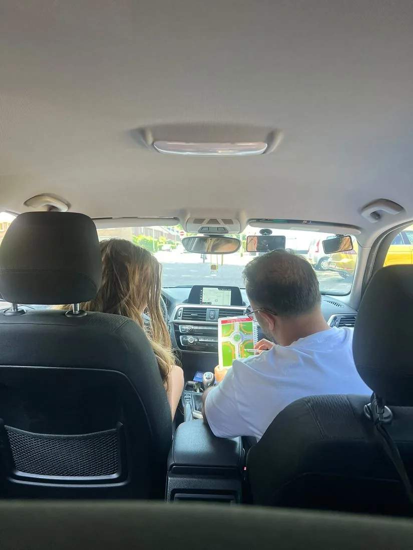 Rijinstructeur legt met een kaart met rotondesituaties uit aan een leerling in de lesauto